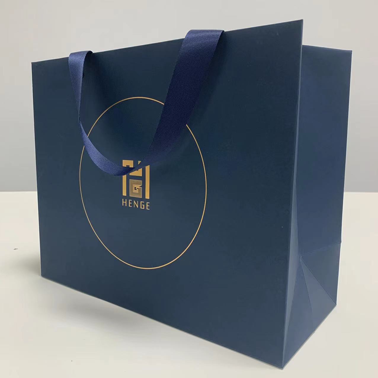 дръжка с панделка на едро, персонализирано отпечатване на лого, луксозна крафт хартиена торба за пазаруване със златно щамповане Представено изображение