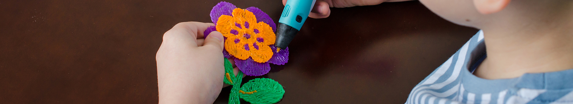 Menino usando caneta 3D.Criança feliz fazendo flor de plástico ABS colorido.