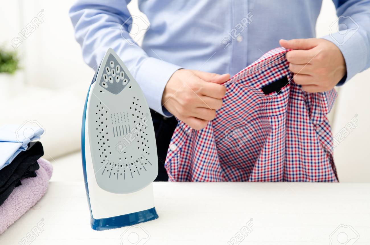 Man ironing shirt on ironing board with steaming blue iron