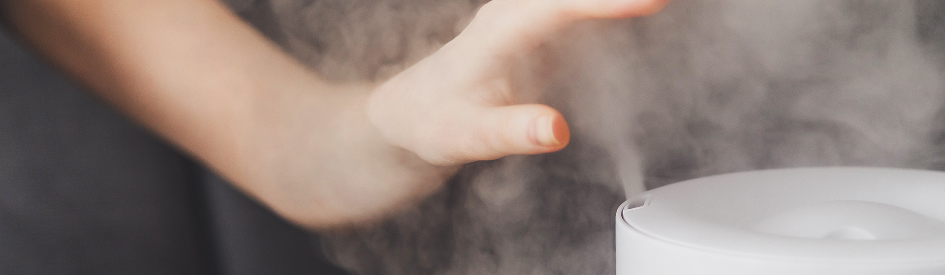Healthy air. The humidifier distributes steam in the living room. Woman keeps hand over vapor